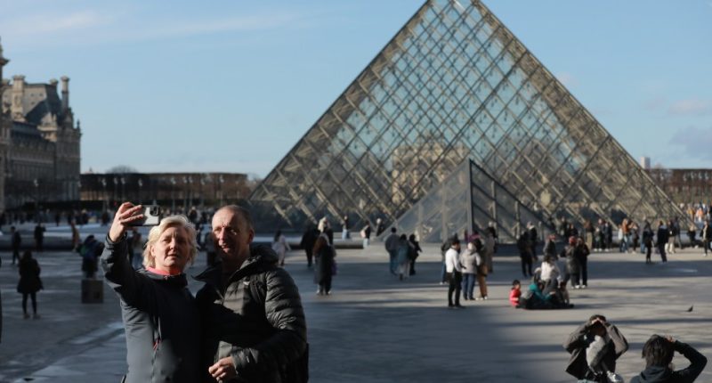 Couple taking a selfie in front of the Louvre Pyramid in Paris.