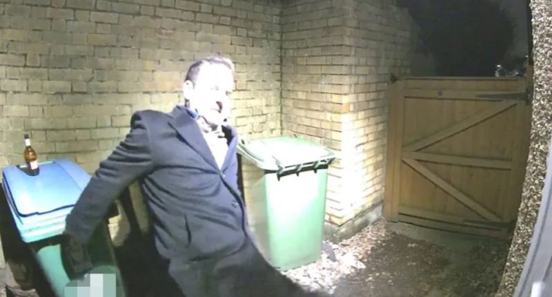 Man leaning against a bin, holding a bottle.