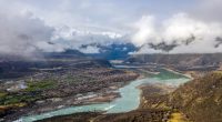Aerial view of the Yarlung Tsangpo River flowing through a valley with snow-capped mountains in the background.