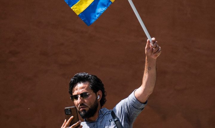 Man holding a Swedish flag and megaphone, using a phone.