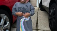 Smiling toddler girl wearing a Pink Floyd shirt and pink shoes.