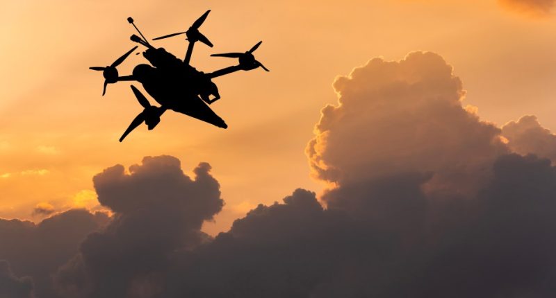 Silhouette of a drone flying in a sunset sky.