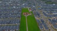 Aerial view of a single house on a large lot surrounded by a new housing development.
