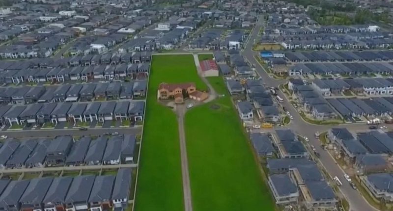 Aerial view of a single house on a large lot surrounded by a new housing development.