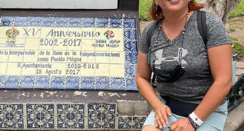 Woman sitting by a plaque commemorating the 15th anniversary of Dolores Hidalgo being named a Pueblo Mágico.