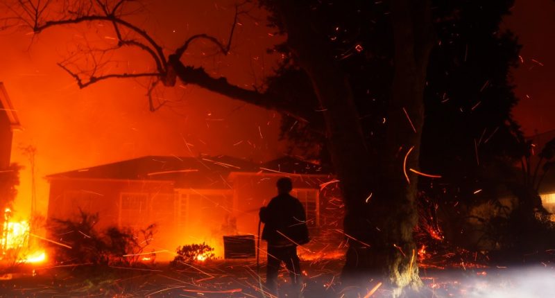 Person hosing down embers from a wildfire near houses.