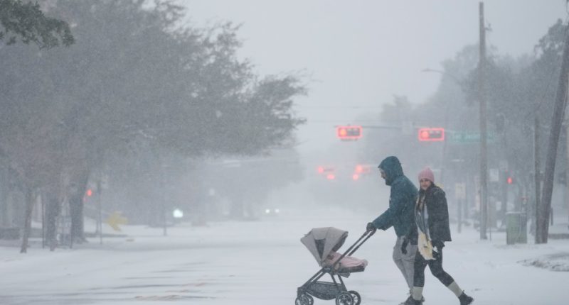 People pushing a stroller walk down a snow-covered street.