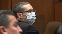 A man wearing glasses and a face mask sits in a courtroom.