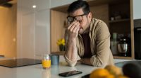 A sad young man sits at a kitchen counter, head in hands.