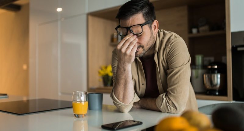 A sad young man sits at a kitchen counter, head in hands.
