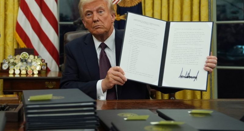 President Trump holding a signed executive order commuting sentences for January 6th offenses.