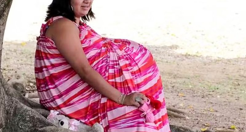 Woman in pink and red striped dress pretending to be pregnant.