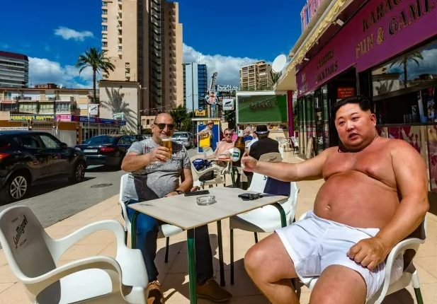 Kim Jong-Un toasting beers with a man at an outdoor cafe.