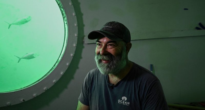 Rudiger Koch, underwater in a room, being interviewed.