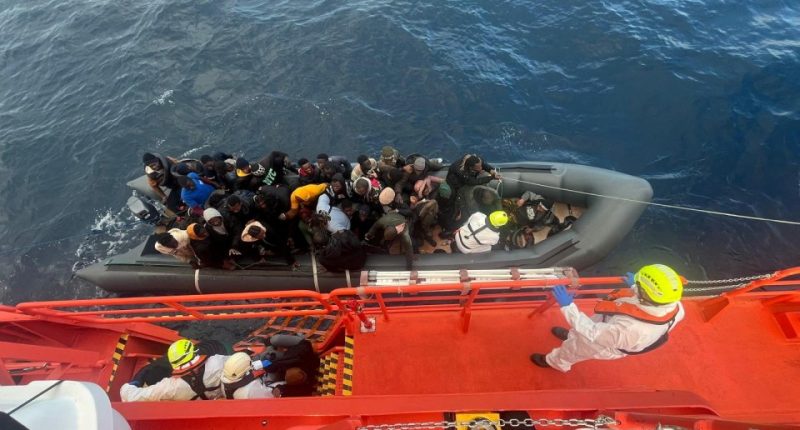 Spanish coast guards wearing white suits work on a rescue operation as they tow a rubber boat carrying migrants, including a newborn baby, off the island