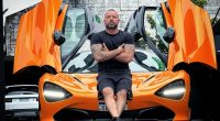Man sitting on an orange McLaren sports car.