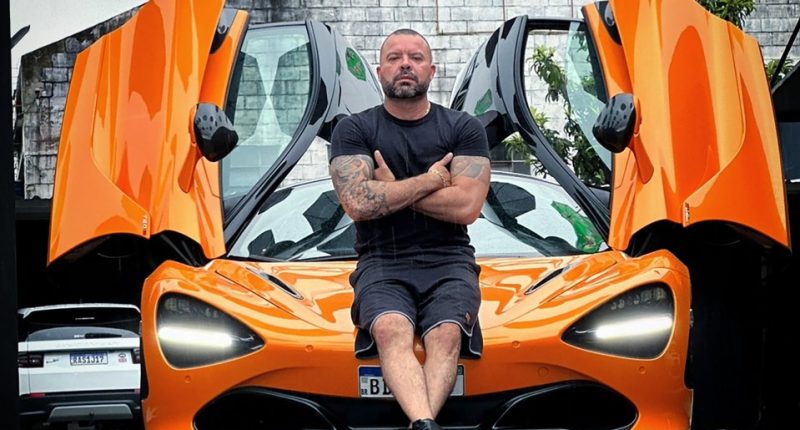 Man sitting on an orange McLaren sports car.