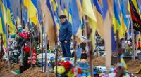 Man mourns at a military cemetery in Kharkiv, Ukraine, among numerous graves marked with Ukrainian flags.