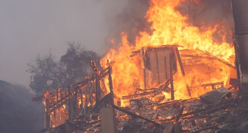 A house engulfed in flames during a wildfire.