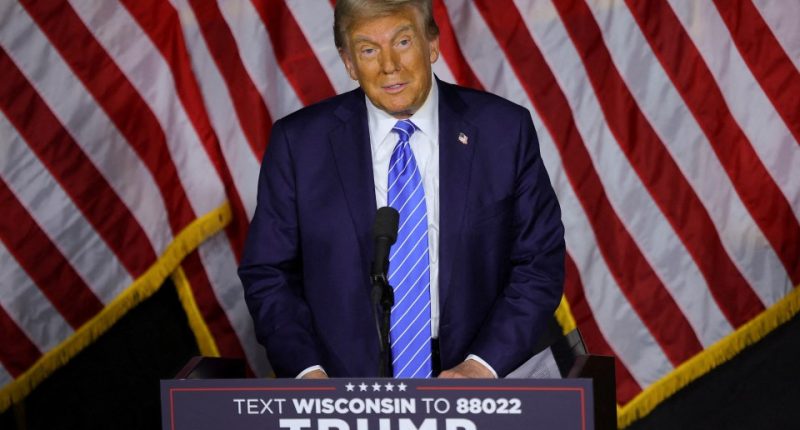 Donald Trump speaking at a podium in front of American flags.