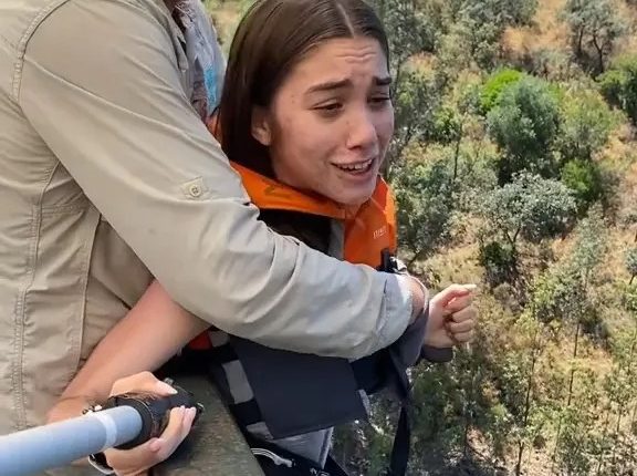 A reluctant woman is pushed off a bridge during a bungee jump.