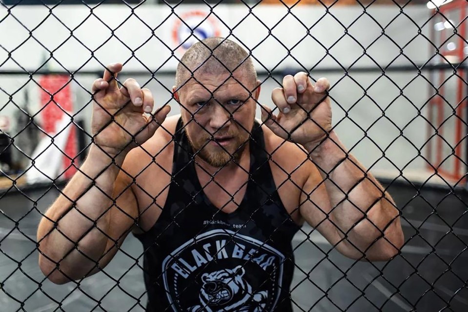 MMA fighter Maxim Novoselov behind a chain-link fence.