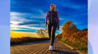 fit, middle-aged woman bundled up and walking on path by the water on fall afternoon at sunset