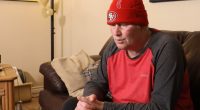 Man in a red San Francisco 49ers beanie and red shirt sits on a couch.