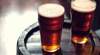 Two pints of bitter ale on a wooden barrel.