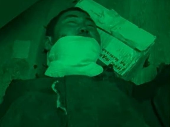 Man lying on the ground with his mouth covered.