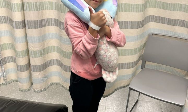 Girl in hospital with neck pillow and stuffed animal.