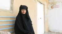 Shamima Begum, a young woman in a niqab, sits on a bench.