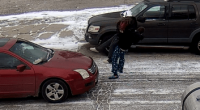 Person carrying another person across a snowy parking lot between two cars.
