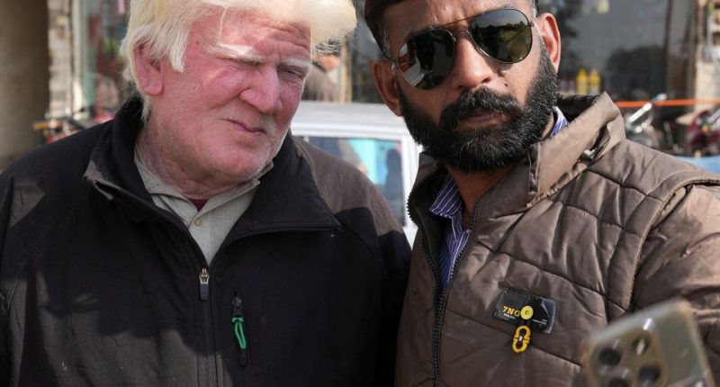 A man taking a selfie with a man who resembles Donald Trump.