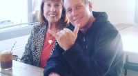 A man and woman sitting at a table together. The man is making a hang loose gesture.