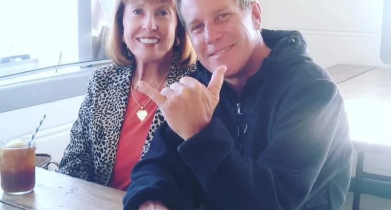 A man and woman sitting at a table together. The man is making a hang loose gesture.
