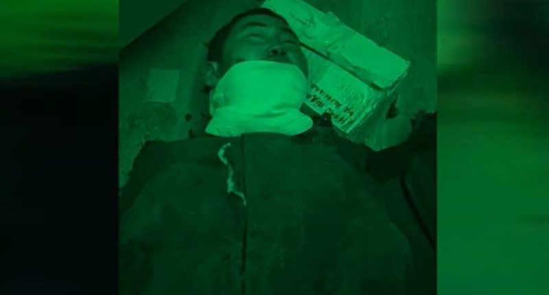 Man lying on the ground with his mouth covered.