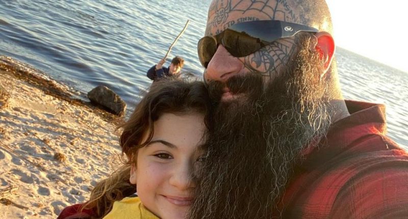 A man hugs a young girl on a beach.