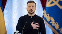 Volodymyr Zelenskyy stands at a podium, hand on heart, during a ceremony in Kyiv.