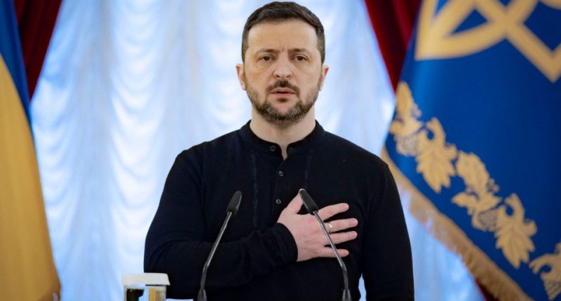 Volodymyr Zelenskyy stands at a podium, hand on heart, during a ceremony in Kyiv.
