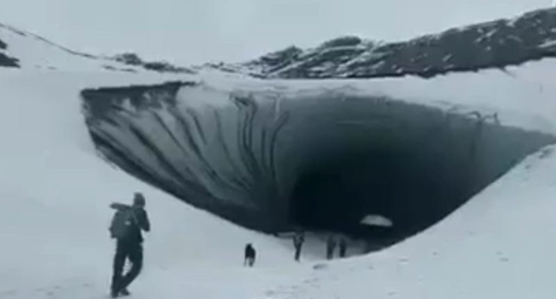 Tourists approach a large ice cave.