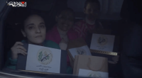 Women in a car holding certificates with a military emblem.
