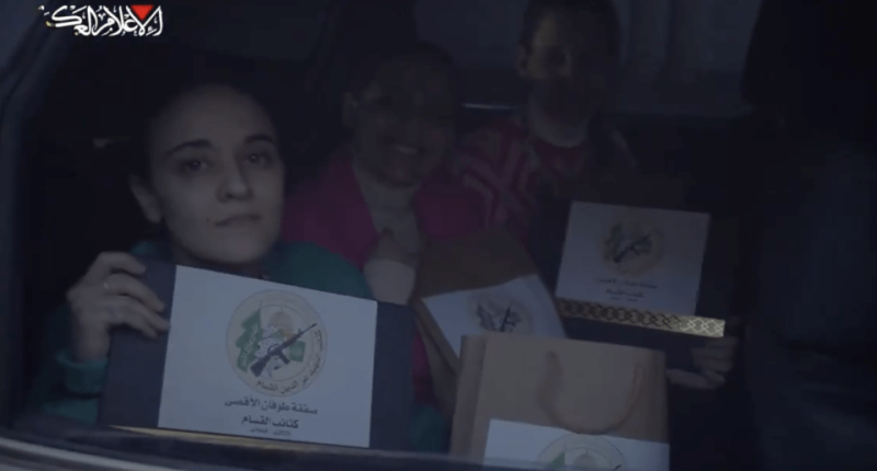 Women in a car holding certificates with a military emblem.