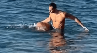 Man helping a dog swim in the ocean.