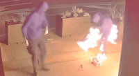 Two hooded figures near a burning object.
