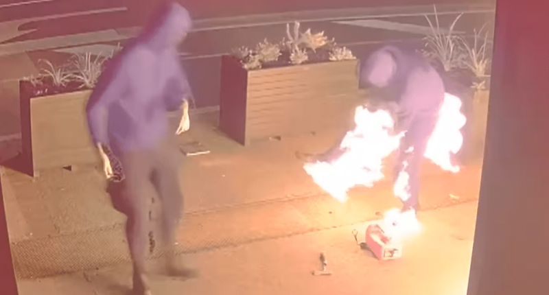 Two hooded figures near a burning object.