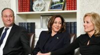 Kamala Harris, flanked by two men, sits in a chair.