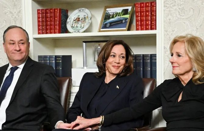 Kamala Harris, flanked by two men, sits in a chair.