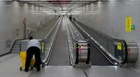 A cleaner with a cart stands at the bottom of a long escalator in a subway station.
