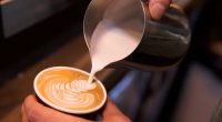 Close-up shot of a barista adding steamed milk to coffee.